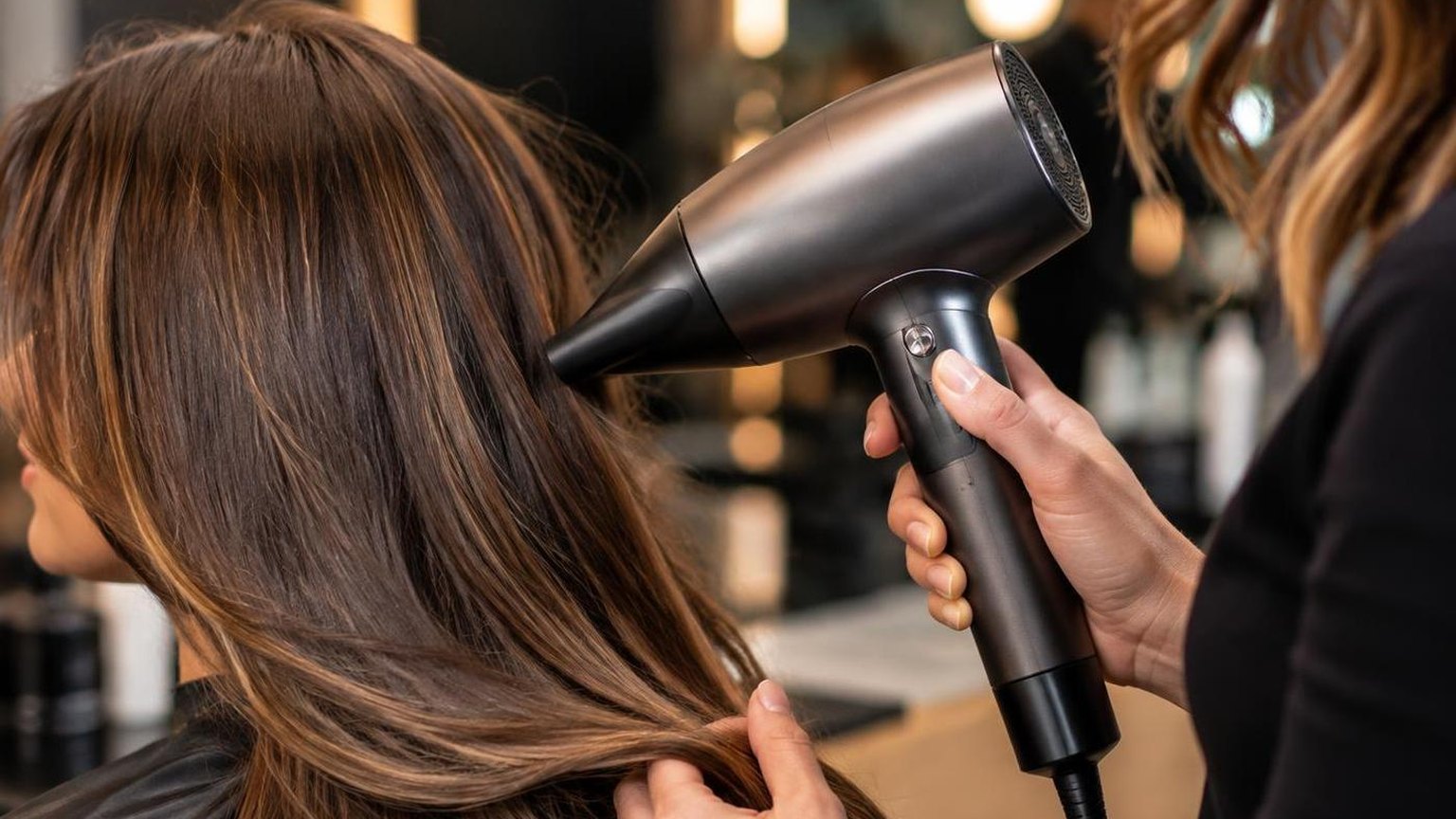 A client at the basin before the blow dry begins, warm light, as it happens at the chair